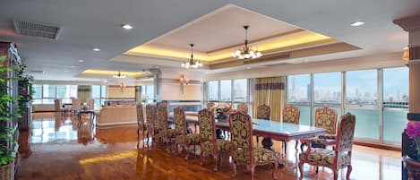 Un comedor espacioso con una larga mesa y sillas ornamentadas, ventanas amplias con vistas a la ciudad y un diseño moderno en el techo.