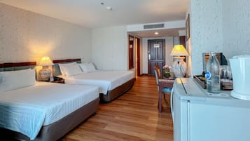 A hotel room with two beds, a desk with a lamp, a coffee maker, and a vase with flowers.
