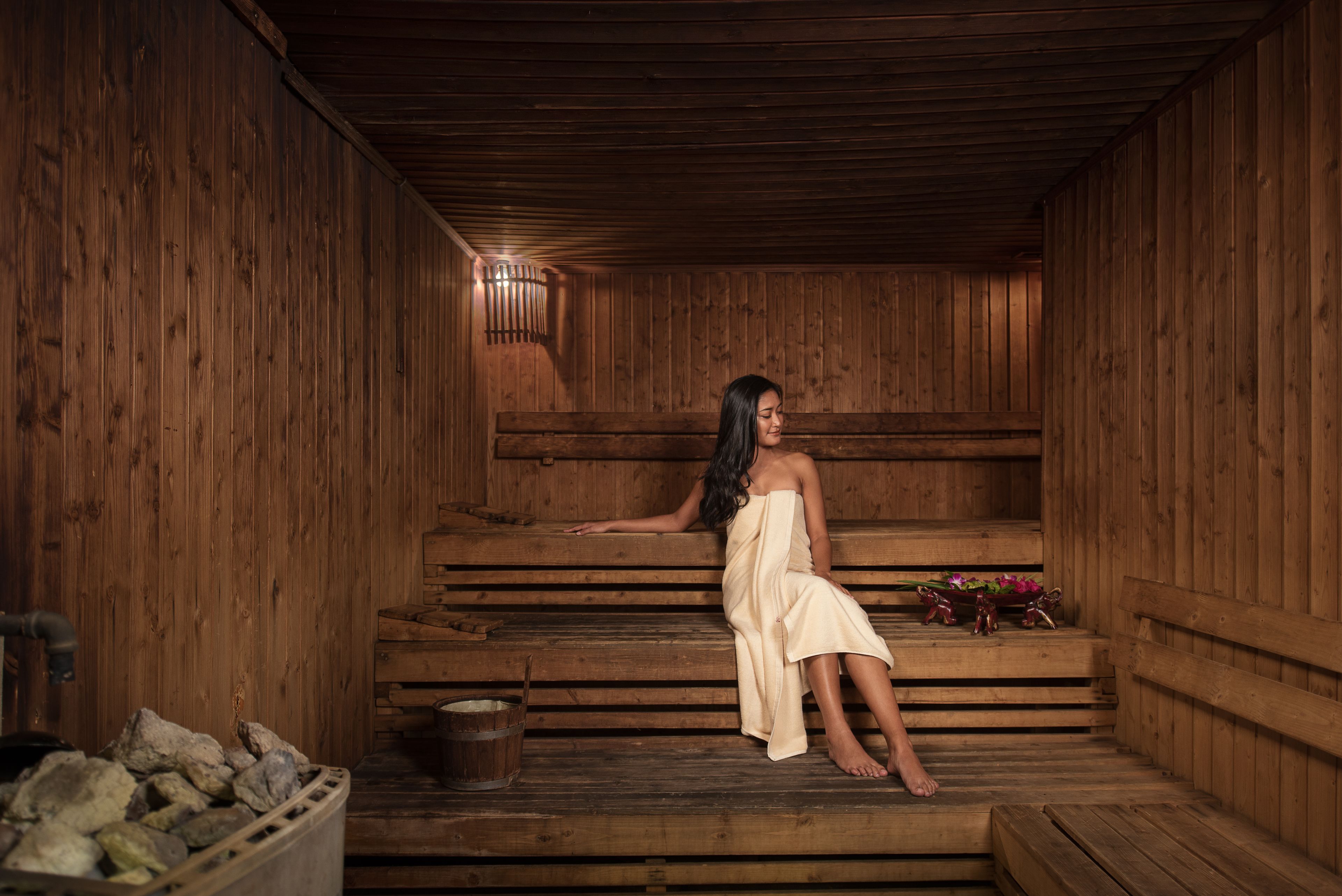 A wooden sauna with benches and a bucket of rocks.