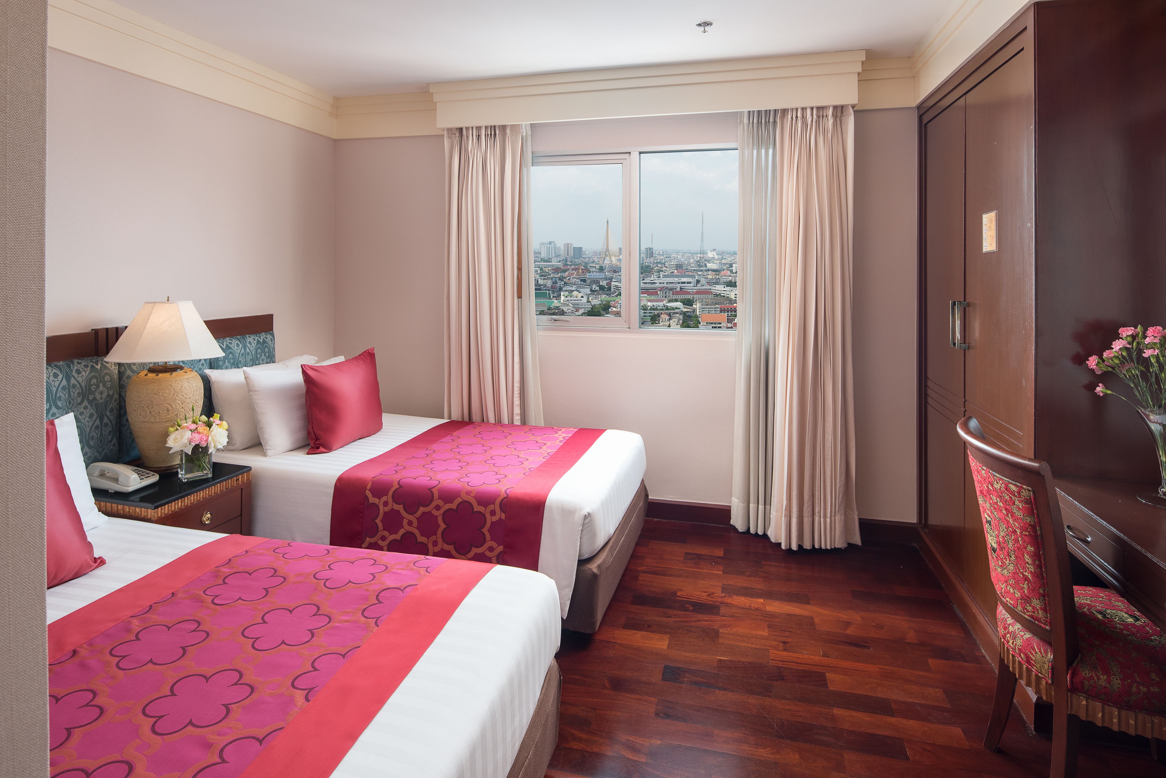 A hotel room with two beds, a nightstand, a desk, a chair, and a large window with a city view.