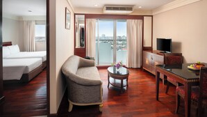 A hotel room with a bed, sofa, dining table, TV, and a balcony with a city view. - Prince Palace Hotel Bangkok (Bangkok)