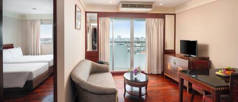Habitación de hotel con cama, sofá, mesa de comedor, televisión y balcón con vistas a la ciudad.