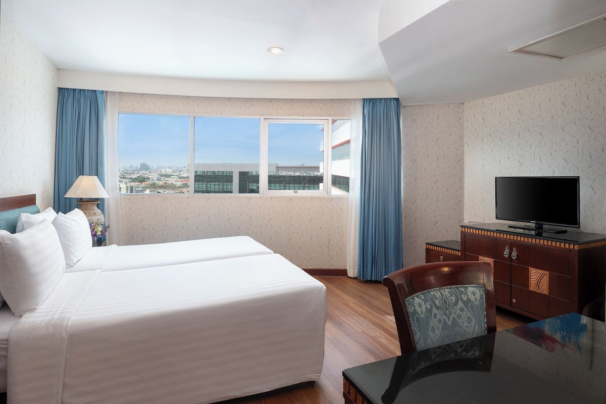 Ein Hotelzimmer mit Bett, Fernseher, Schreibtisch und Fenster mit Blick auf die Stadt.