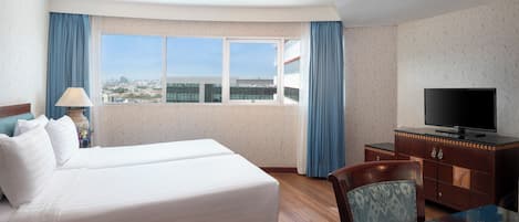 A hotel room with a bed, a TV, a desk, and a window with a city view.