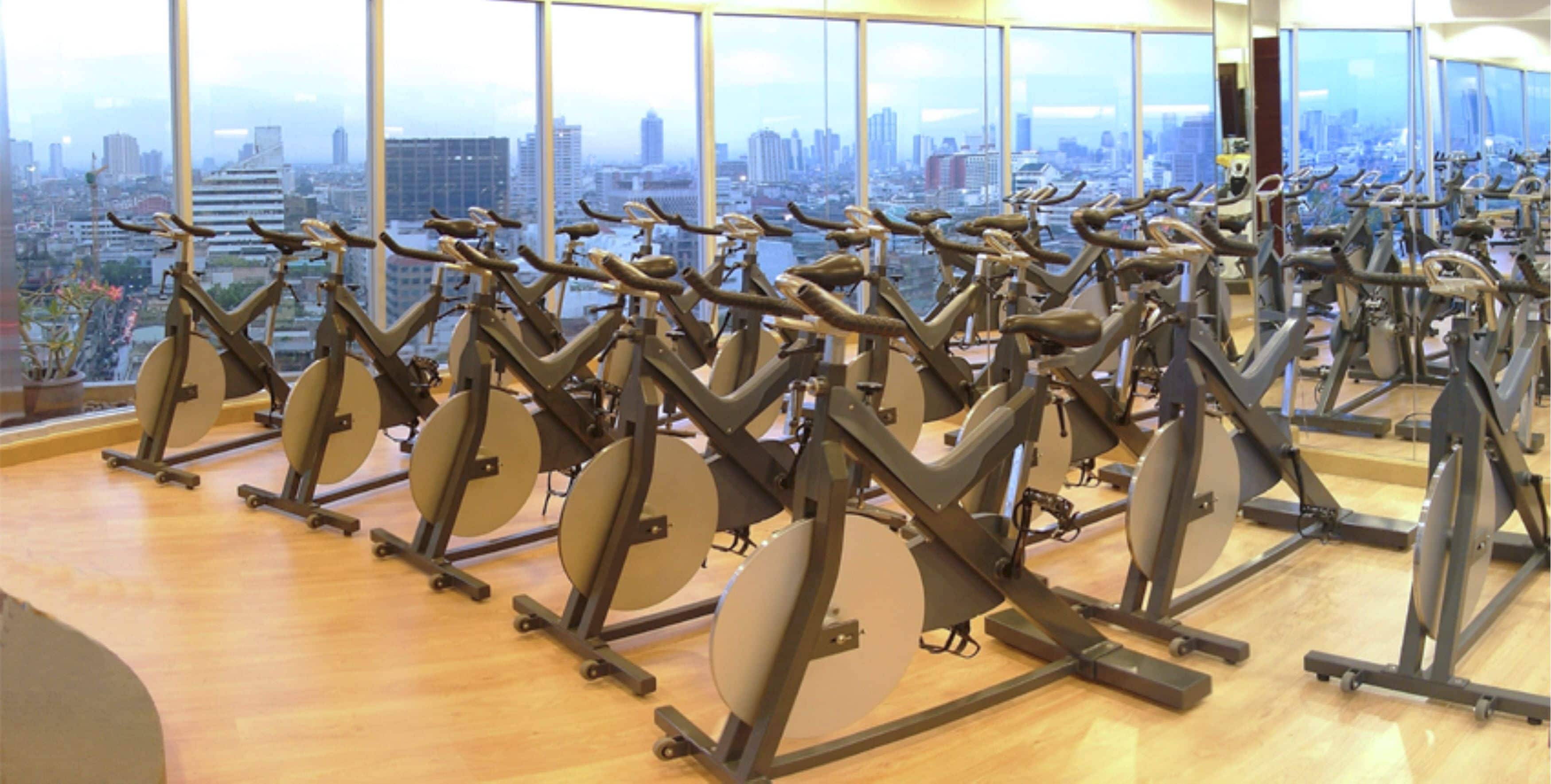 A gym with stationary bikes arranged in rows, large windows offering a city view.