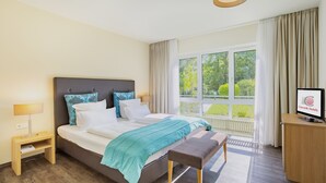 Hotelkamer met een bed, nachtkastje, bankje, televisie en een raam met uitzicht op groen.