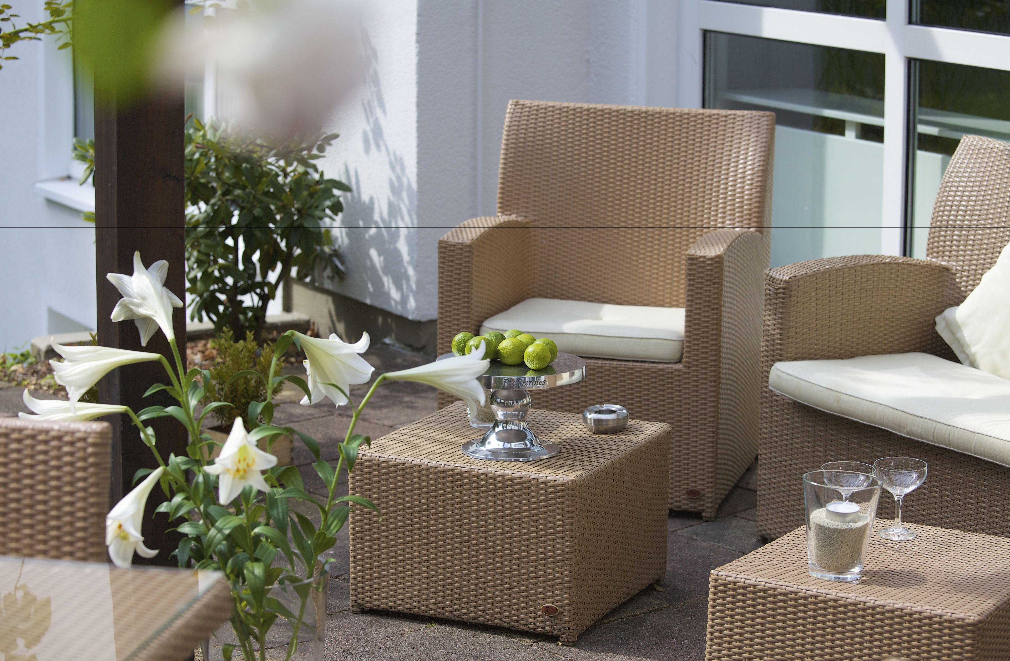 Wicker furniture with cushions, a table with a decorative item, and a potted plant with white flowers.