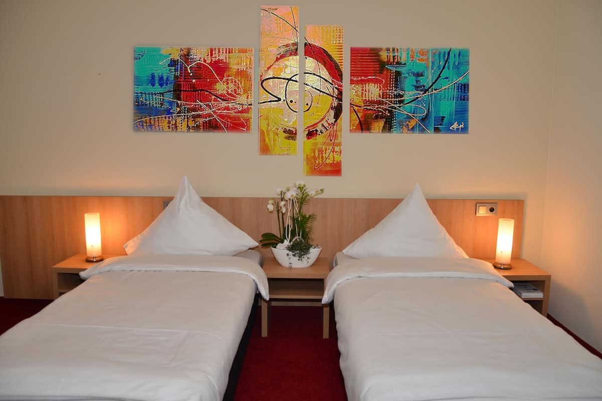 A hotel room with two beds, a wooden headboard, bedside lamps, and a wall with abstract art.