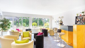 Een moderne lounge met comfortabele zitplaatsen, een bar met diverse flessen en grote ramen met uitzicht op groen.