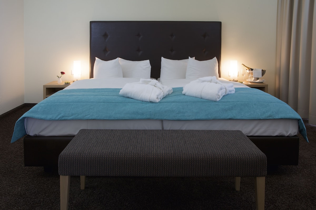 A neatly made bed with white and teal bedding, a dark headboard, and a matching bench in front.