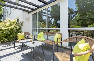 Um pátio externo com móveis de vime, uma mesa e uma estrutura de vidro.