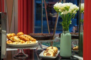 A display of pastries and desserts on a glass table with a vase of flowers. - Casual Eclettico Milano Hotel by Casual Hoteles (Milan)