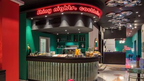 Eine hell erleuchtete Frühstücksbar mit leuchtendem Neonlicht, einer Auswahl an Frühstücksartikeln und einer Sitzgegend mit Tischen und Stühlen.