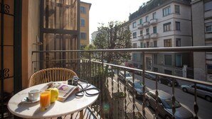 Ein Balkon mit Tisch, Stühlen und einer Zeitung. Darunter sind Autos in der Straße geparkt.