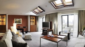 Une chambre d’hôtel dotée d’un espace salon comprenant un canapé, des fauteuils, une table basse, un téléviseur et un balcon avec des rideaux.