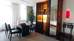 Une chambre d’hôtel équipée d’un bureau, de chaises, d’une plante en pot, d’un lit, d’un miroir et d’une lampe murale rouge.