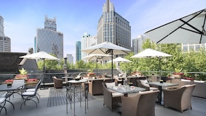 Une terrasse extérieure aménagée avec des meubles en osier, des parasols et, en arrière-plan, une vue sur les toits de la ville.
