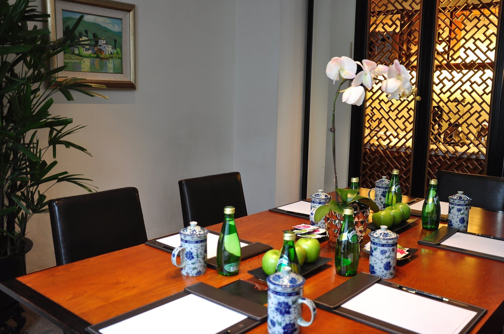 Una mesa de conferencias con un florero, botellas verdes y un cuadro en la pared.