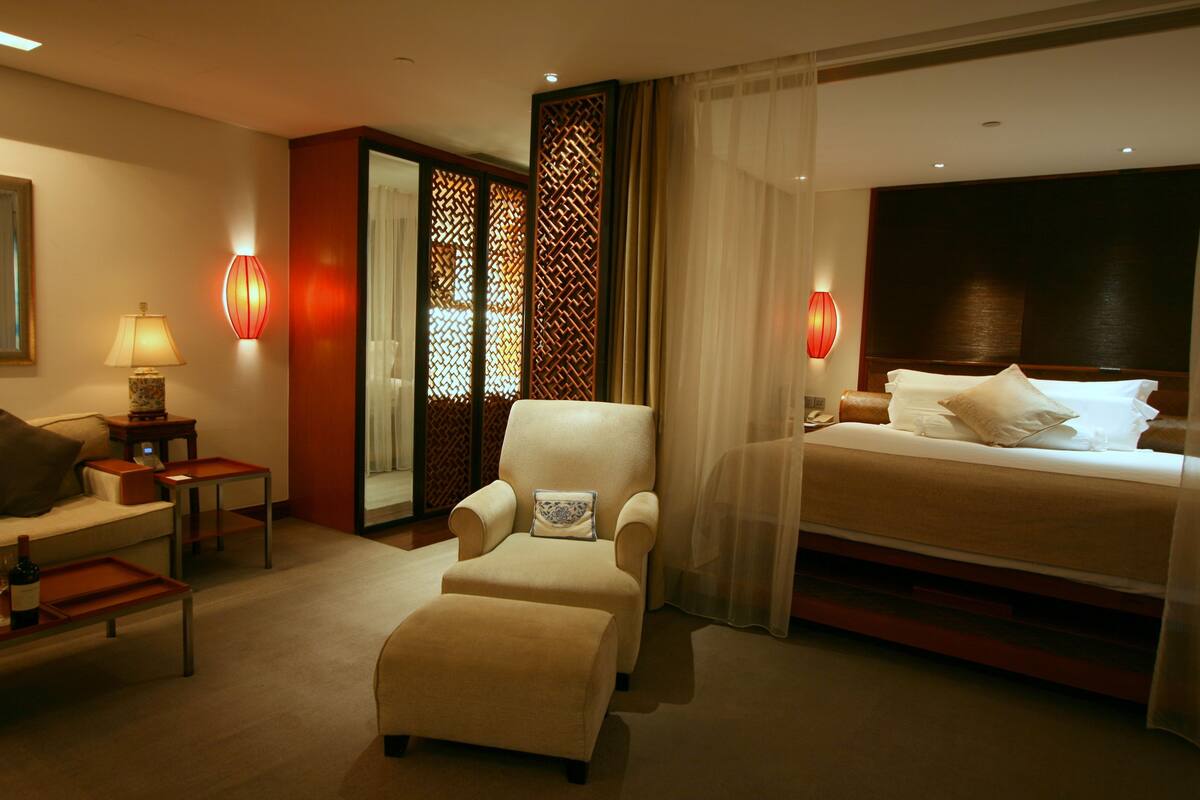 Habitación de hotel con cama, sofá, silla, una mesita y un separador decorativo.
