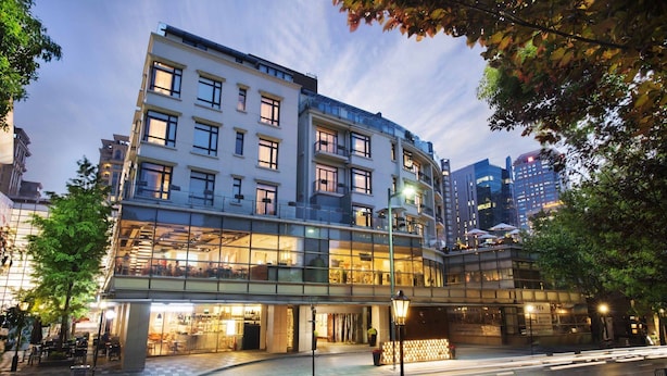 Un hôtel à plusieurs étages doté d’une façade en verre, d’un espace extérieur aménagé pour s’asseoir et d’un pont piétonnier.