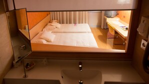Una habitación de hotel con cama, mesita de noche, espejo, lavamanos y ventana.