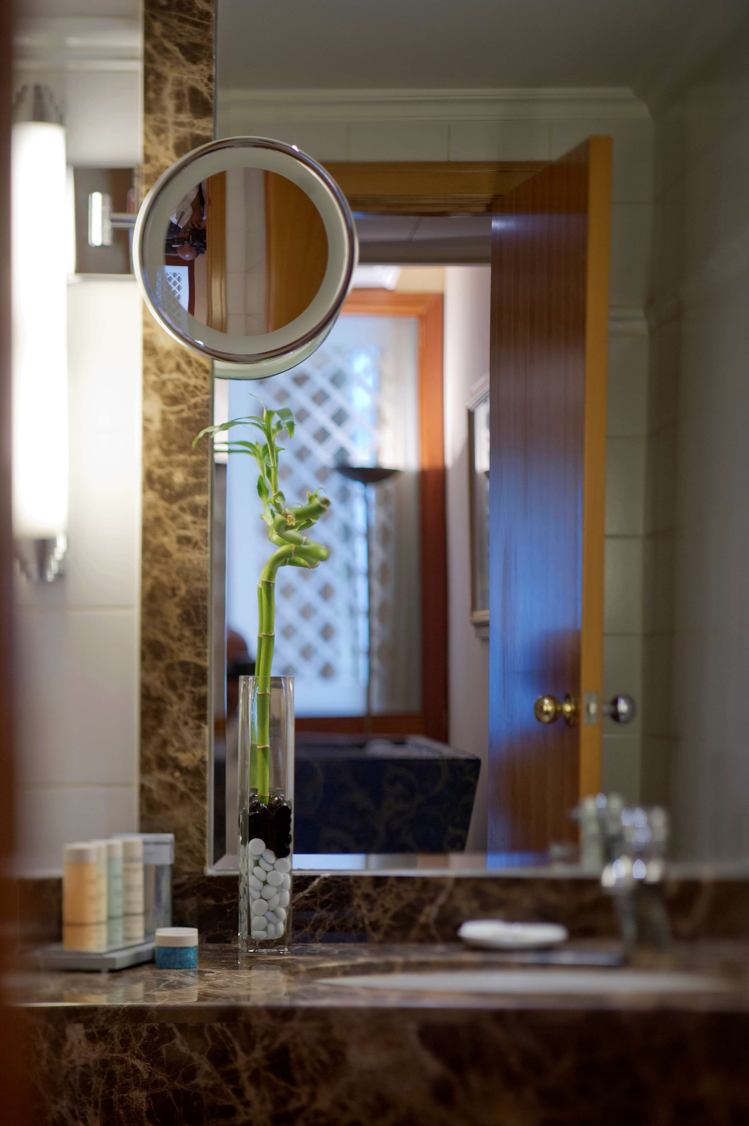 A bathroom vanity with a marble countertop, a glass vase with a plant, and a mirror above it.