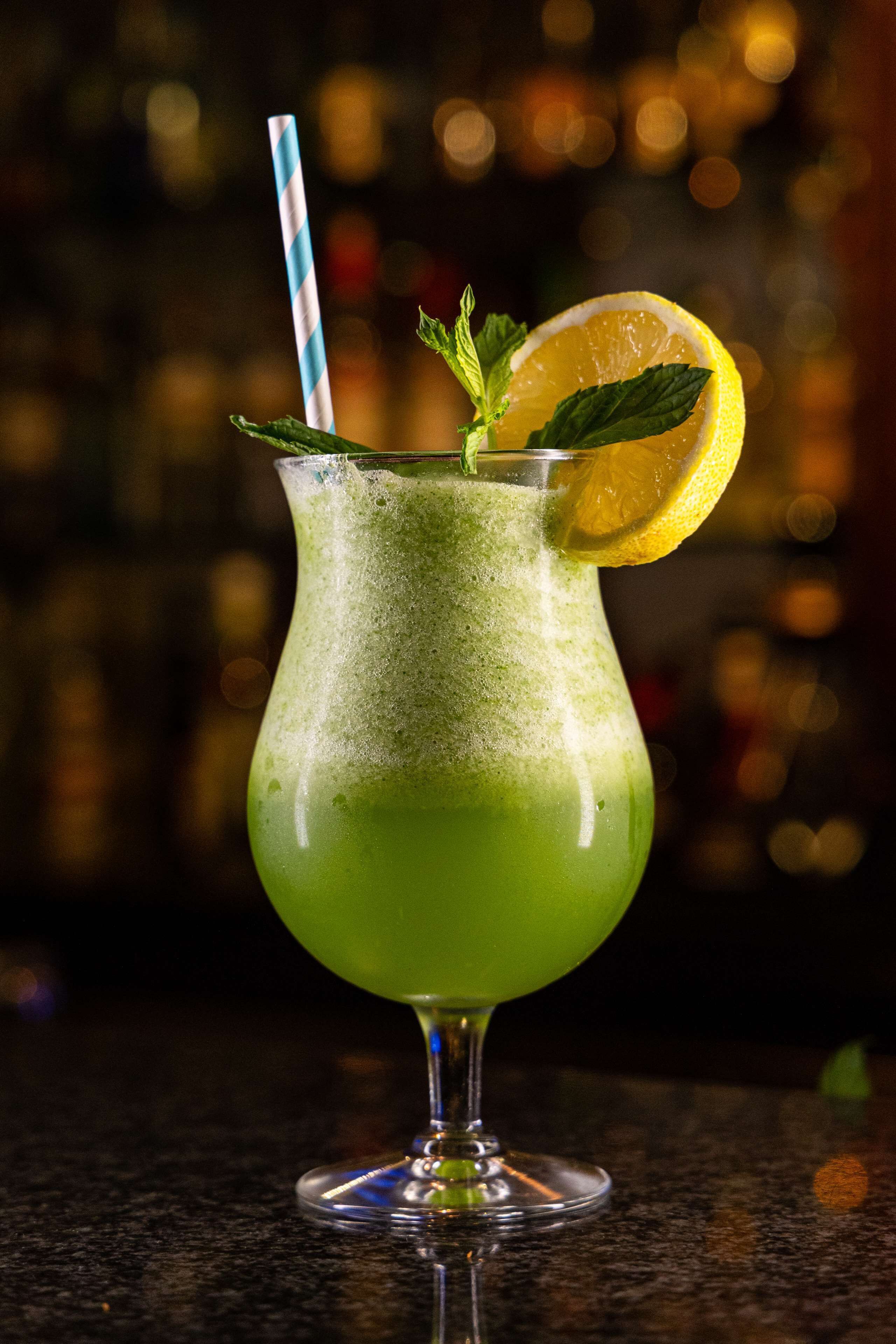 Un cóctel verde en un vaso con pajita a rayas y una rodaja de limón.