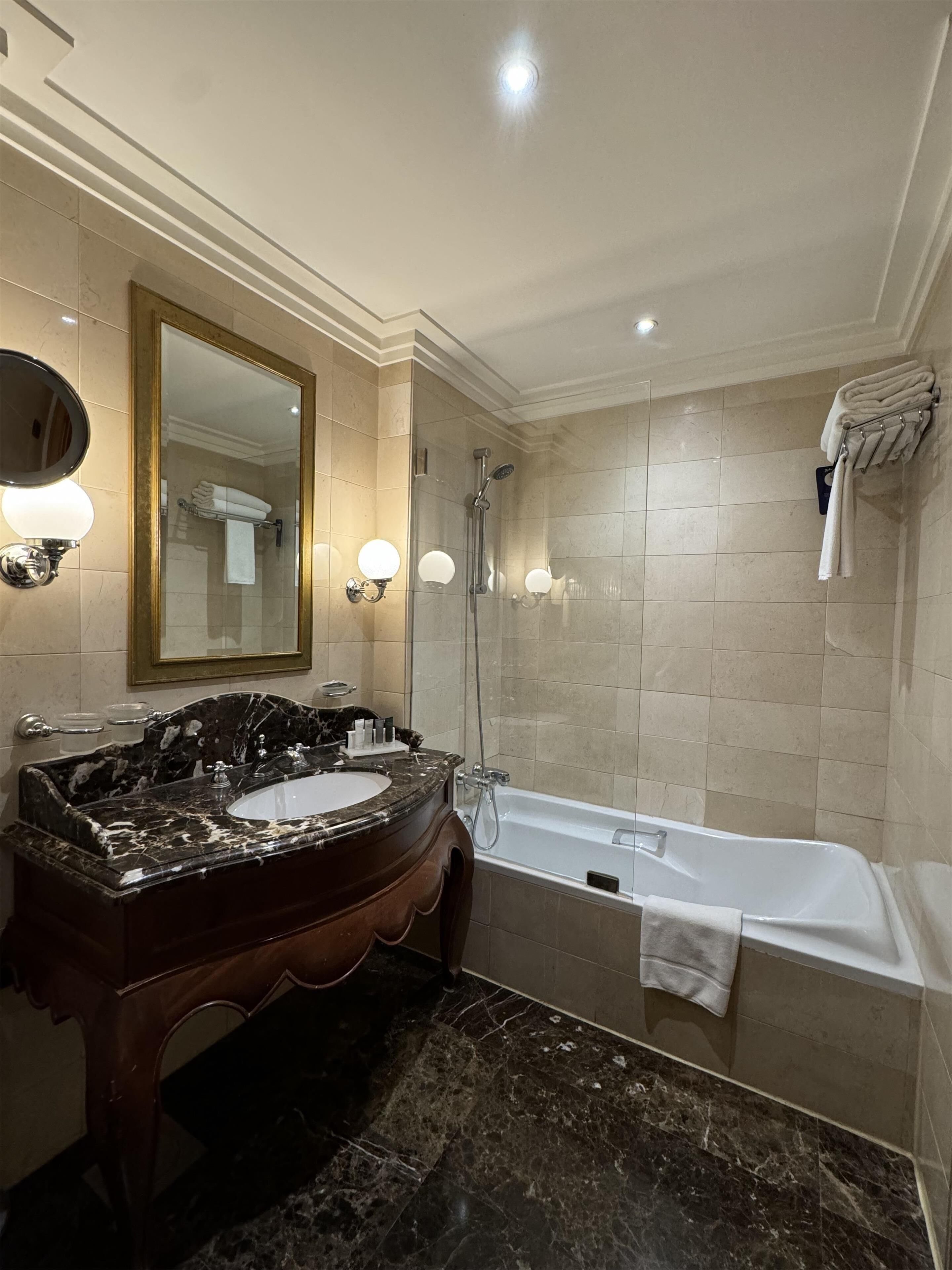 A bathroom with a marble vanity, a large mirror, a bathtub, and a glass-enclosed shower.