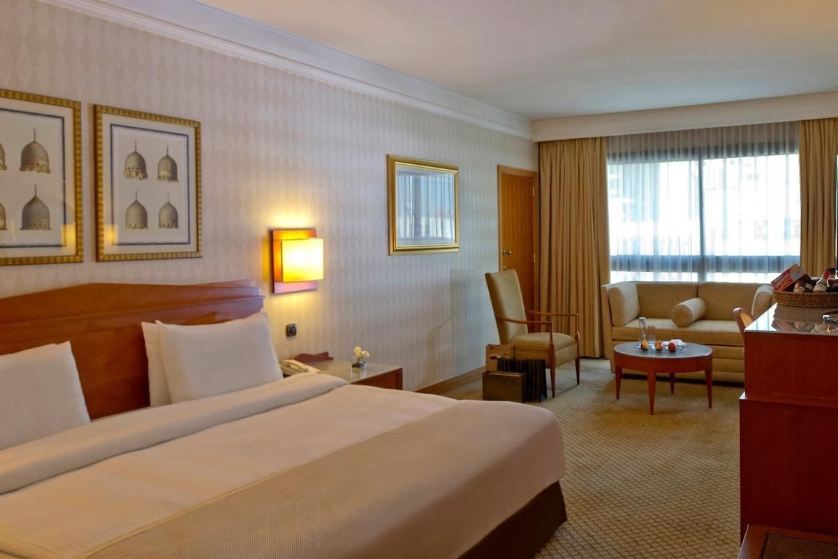 A hotel room with a large bed, two armchairs, a sofa, a desk, and a window with curtains.
