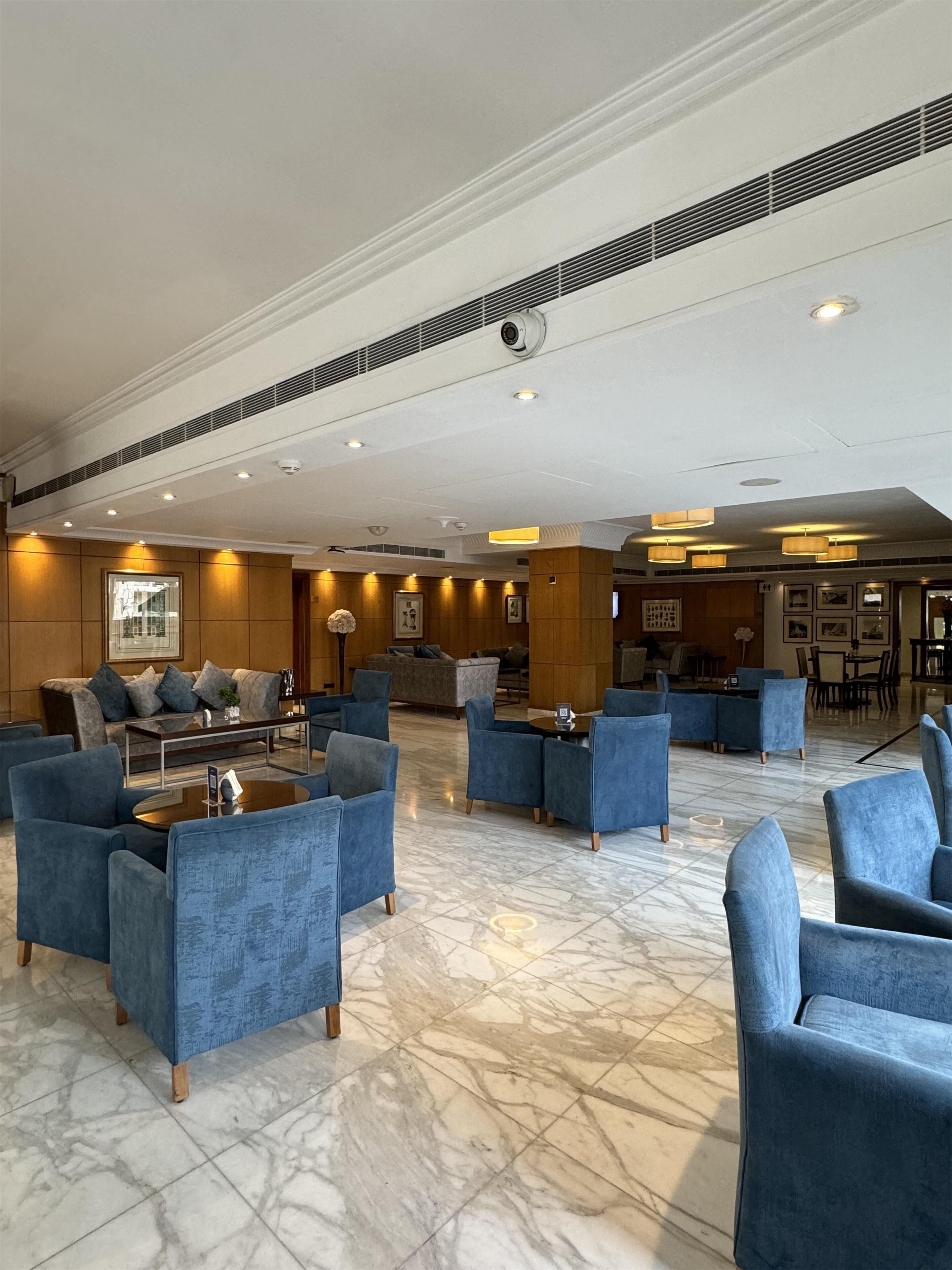Eine großzügige Lobby mit Marmorböden, blau gepolsterten Sitzmöglichkeiten und einem modernen Deckenbau.