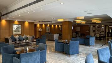 Eine großzügige Lobby mit Marmorböden, blau gepolsterten Sitzmöglichkeiten und einem modernen Deckenbau.