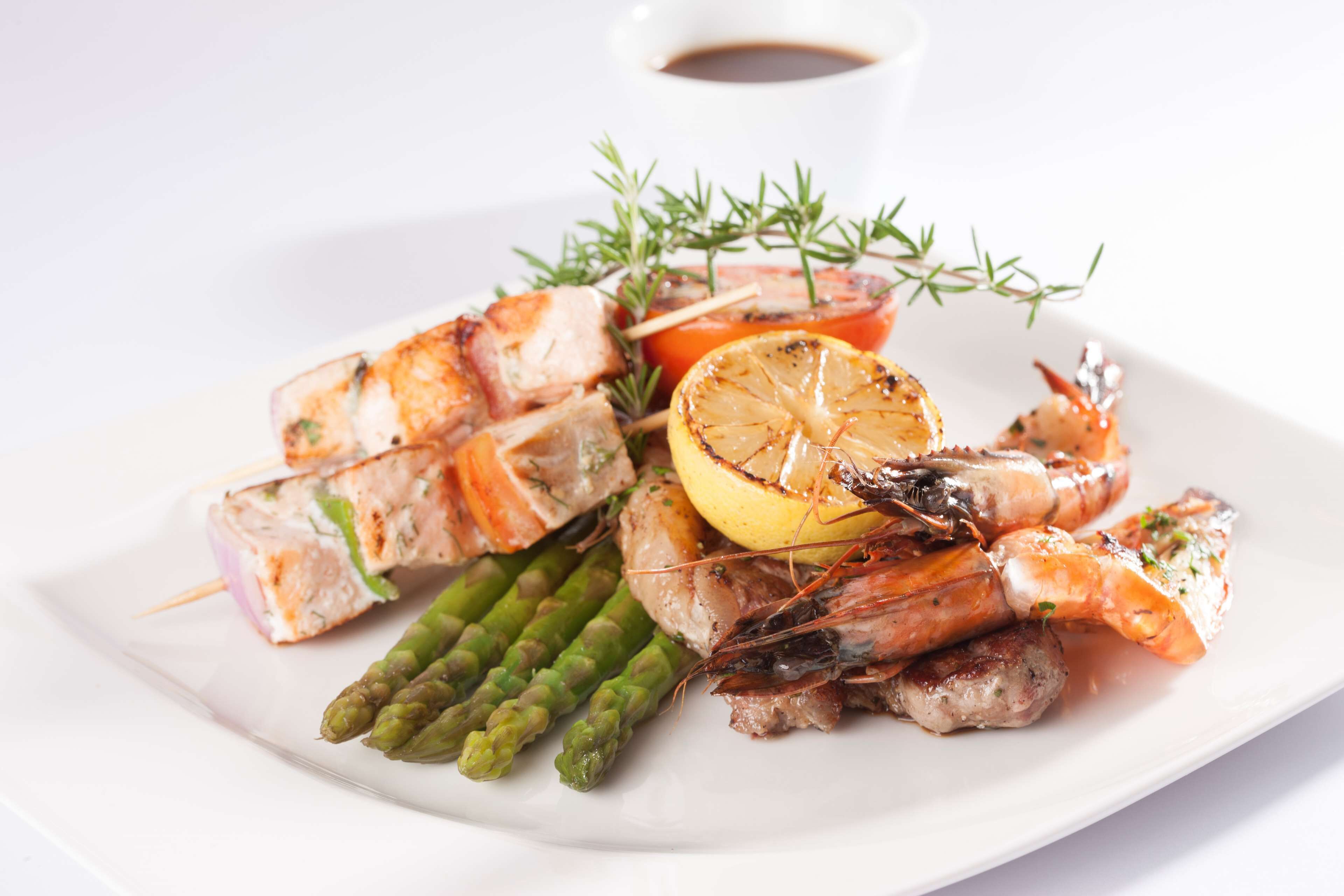 Un plato de mariscos a la parrilla, que incluye camarones, espárragos y rodajas de limón, adornado con hierbas.