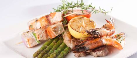 Un plato de mariscos a la parrilla, que incluye camarones, espárragos y rodajas de limón, adornado con hierbas.