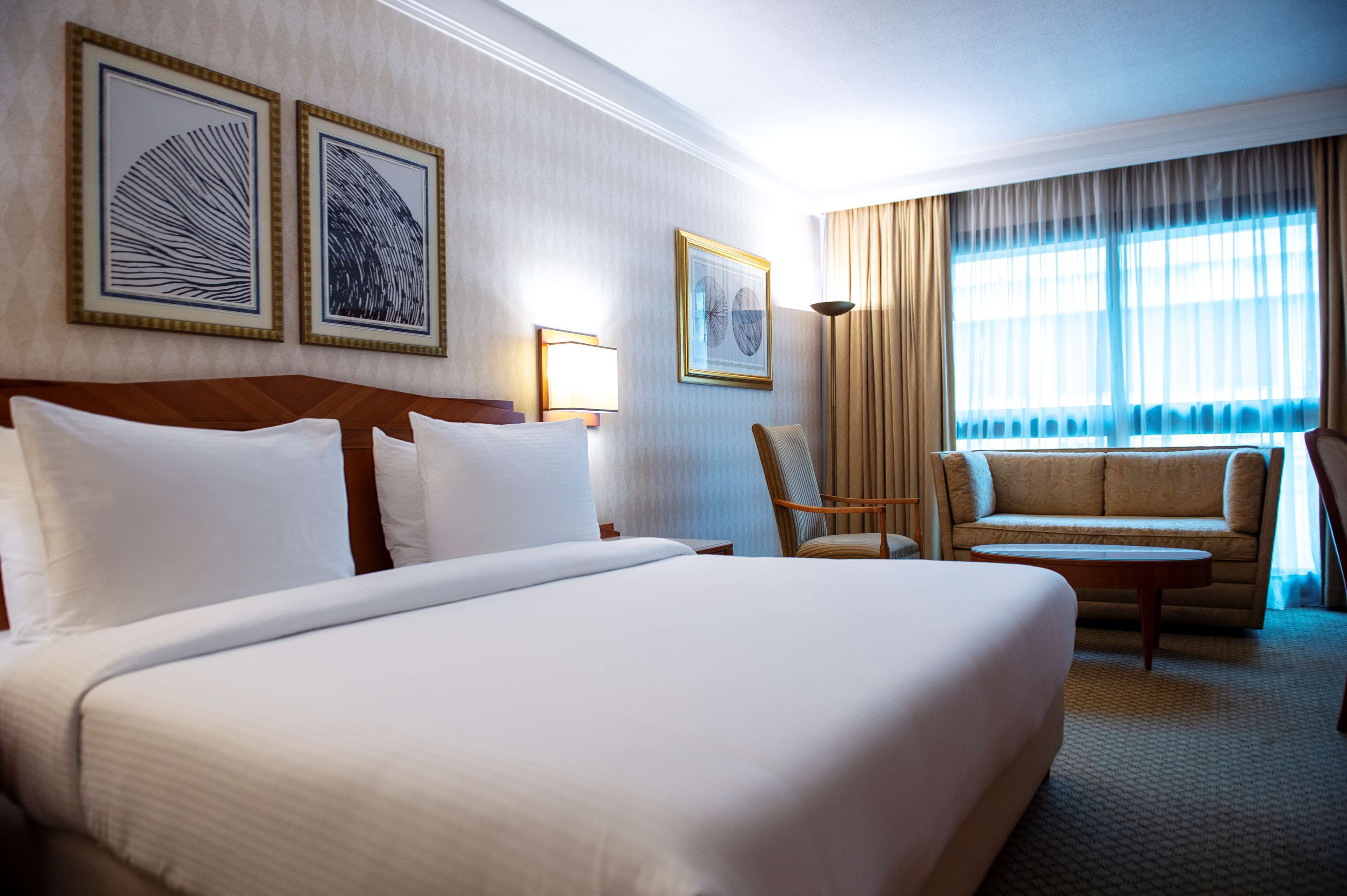 Una habitación de hotel con una cama grande, un sofá, una silla y dos cuadros en la pared.