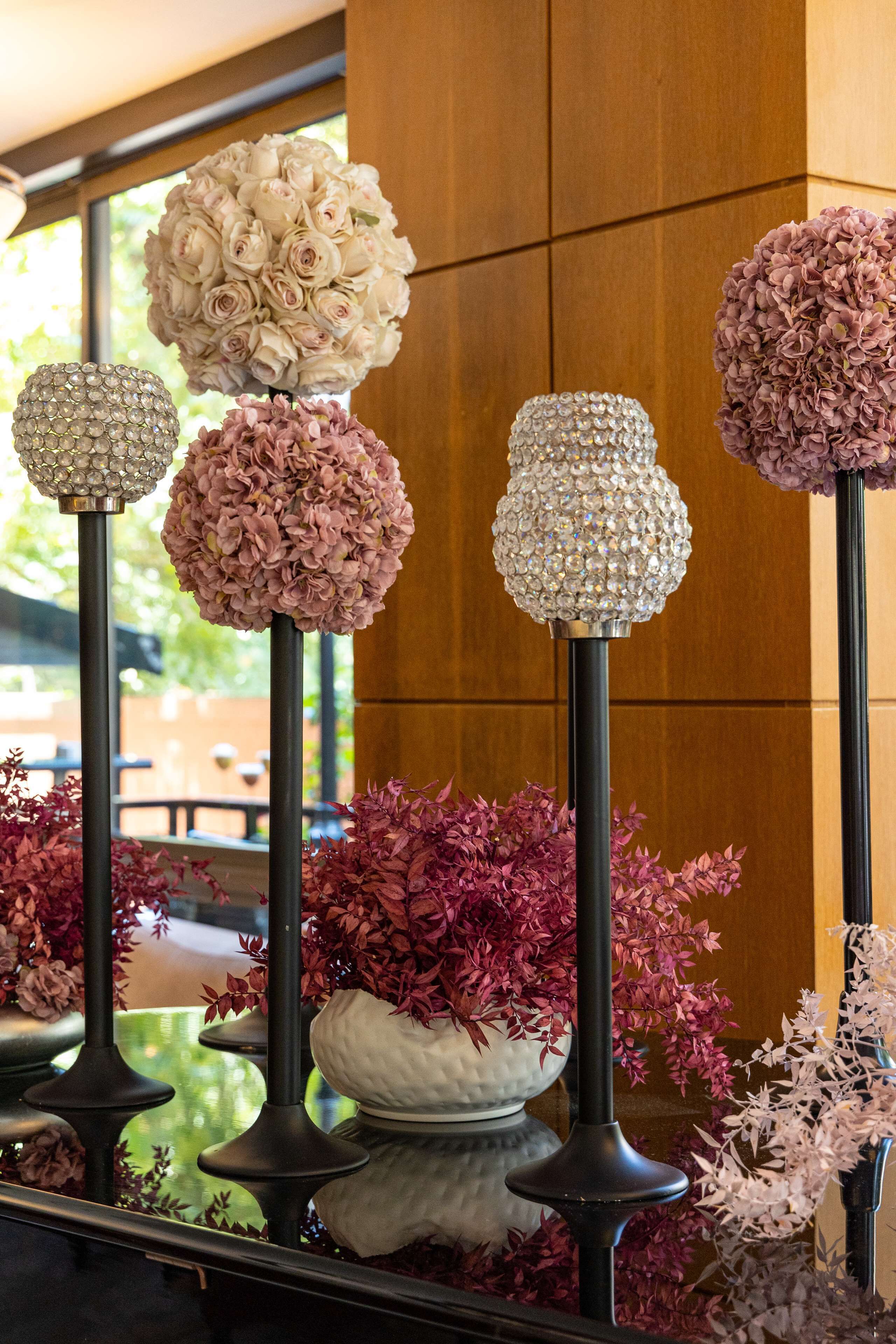 Une rangée d’appliques décoratives dotées de globes en cristal, placées sur un mur en bois et entourées de différentes plantes en pot.