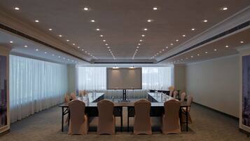 A conference room with a long table, chairs, a projector screen, and a large window with blinds.