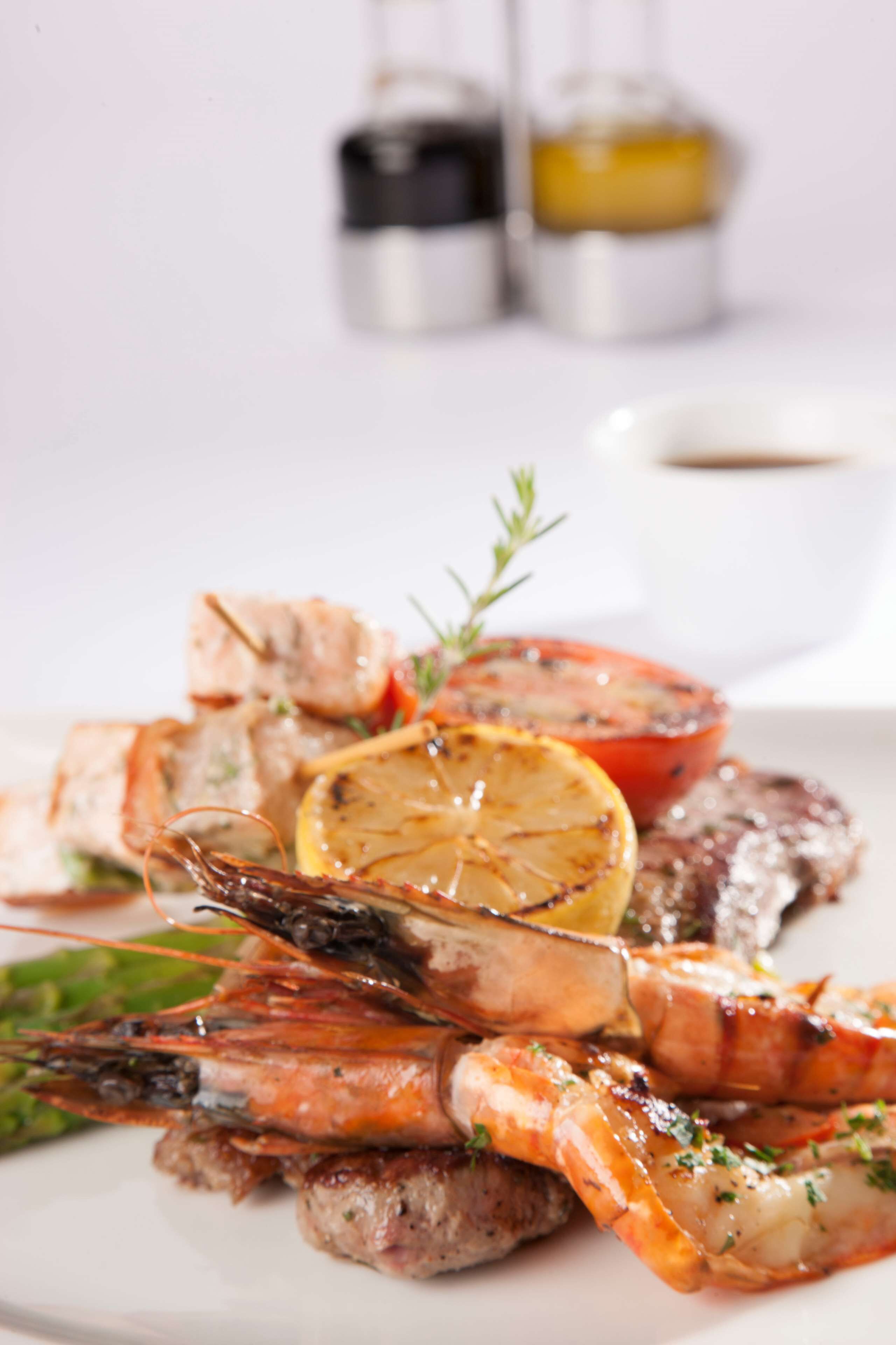 A plate of grilled seafood including shrimp, fish, and vegetables, with a small bowl of sauce.