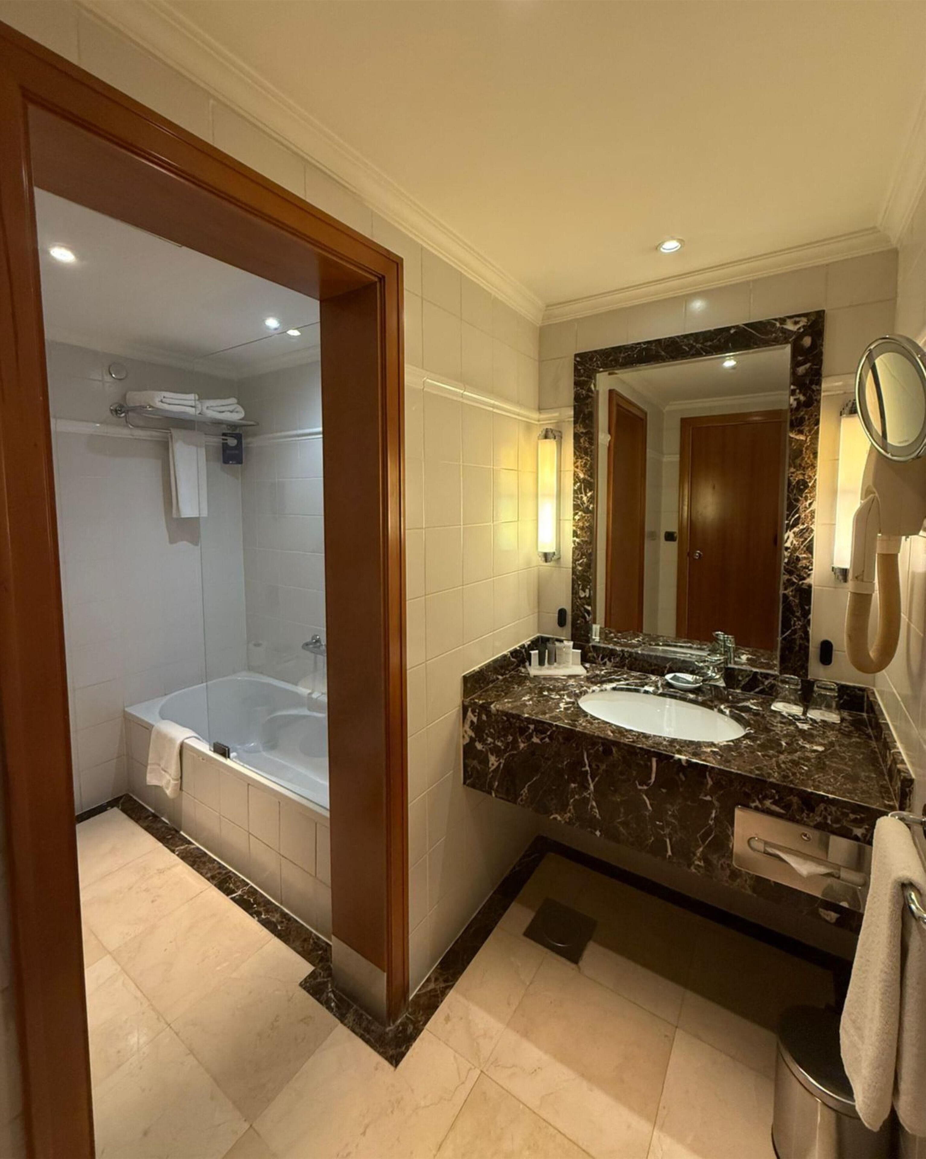 Un baño moderno con bañera, lavamanos con encimera de mármol y un espejo grande.