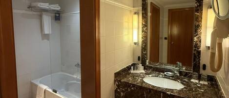 Un baño moderno con bañera, lavamanos con encimera de mármol y un espejo grande.