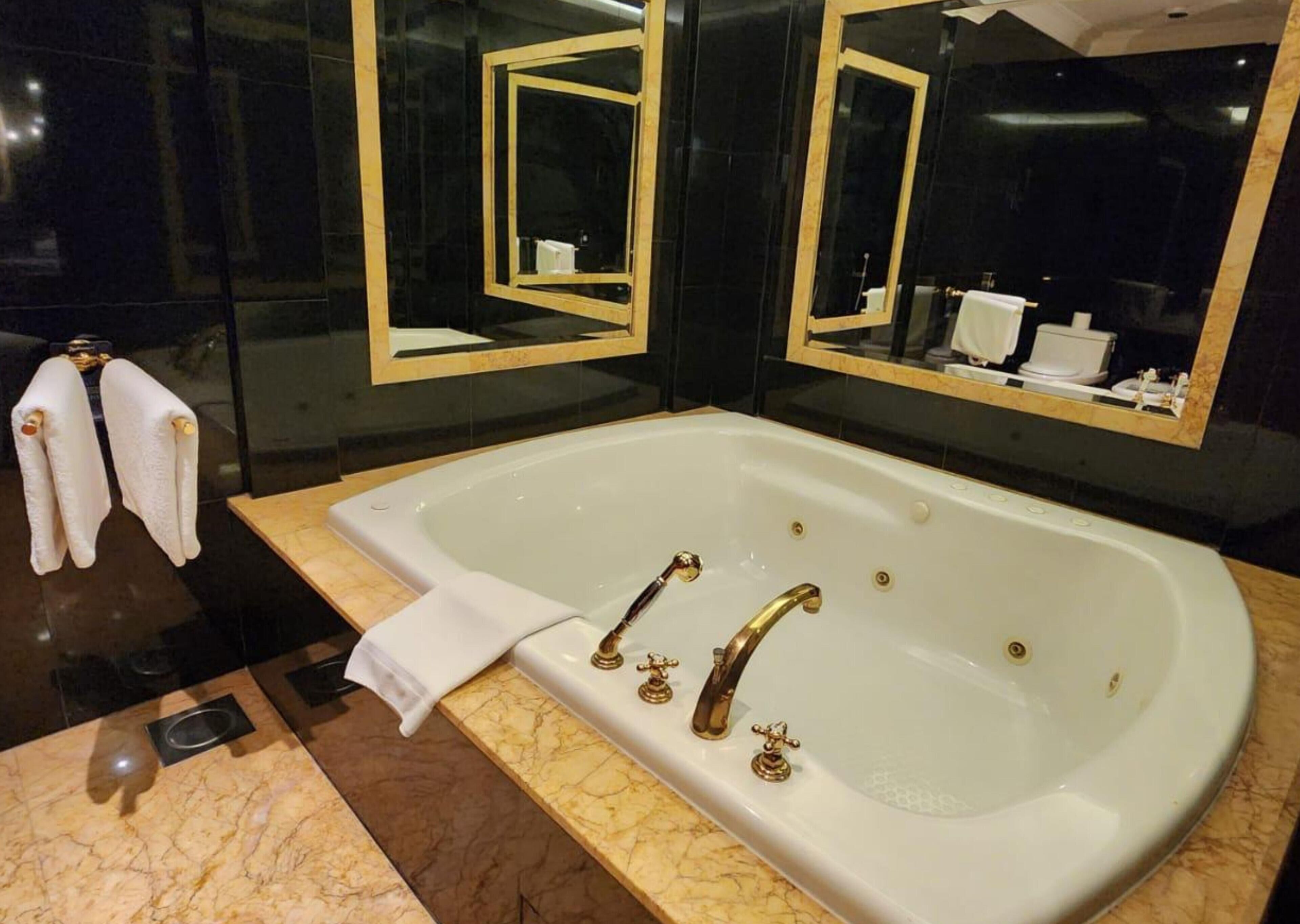 A modern bathroom with a large bathtub, two mirrors, and a marble countertop.