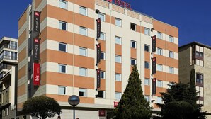 Un hôtel à plusieurs étages, portant l’enseigne « ibis HOTEL », qui se distingue par une architecture moderne aux couleurs beige et marron, de nombreuses fenêtres et des balcons.
