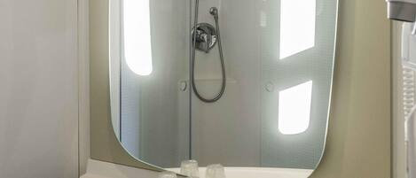 A bathroom with a large mirror, a shower, and a sink with a faucet.