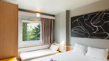 Une chambre d’hôtel avec un lit, une fenêtre avec des rideaux, une table de chevet avec une lampe et une œuvre d’art décorative au mur.