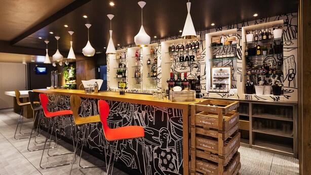 Un espace bar avec un comptoir, des tabourets et des étagères remplies de bouteilles et de verres.
