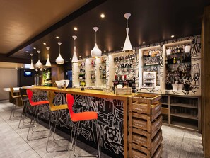 Una zona de bar con mostrador, taburetes y estantes llenos de botellas y vasos.