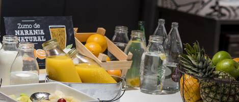 Una mesa de desayuno con un tazón de fruta, un vaso de jugo de naranja y una botella de leche.