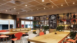 L’intérieur d’un restaurant se caractérise par un plafond haut, un plafond à motifs géométriques et un tableau affichant le menu sur un mur.