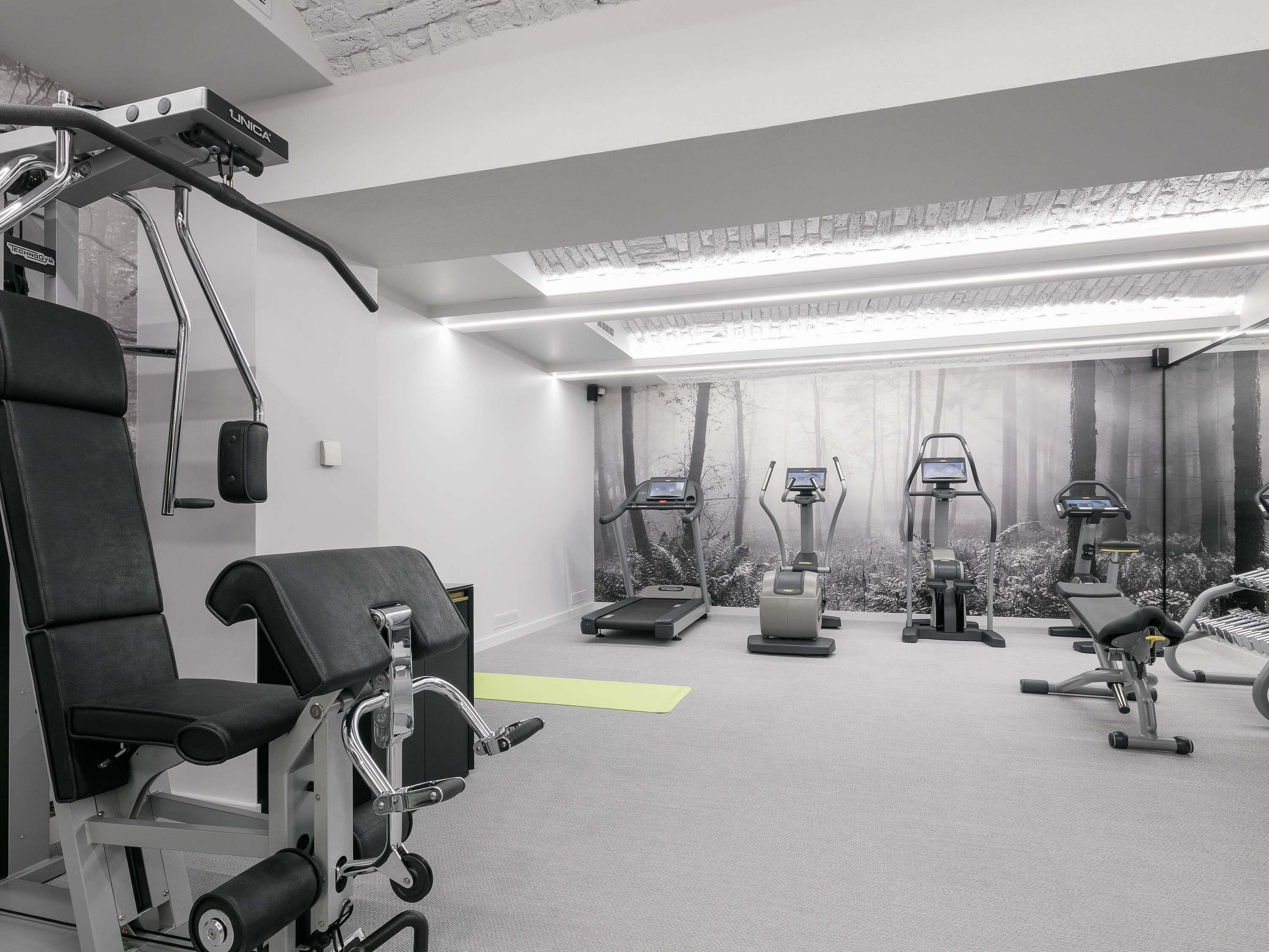 A gym with various exercise equipment, including treadmills and weight machines, and a wall mural of a forest.