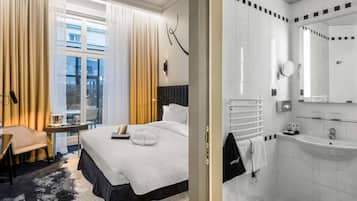 Una camera d'albergo con un letto, un comodino con una lampada, una finestra con tende, un bagno con un lavandino e uno specchio, e un pavimento a scacchi.
