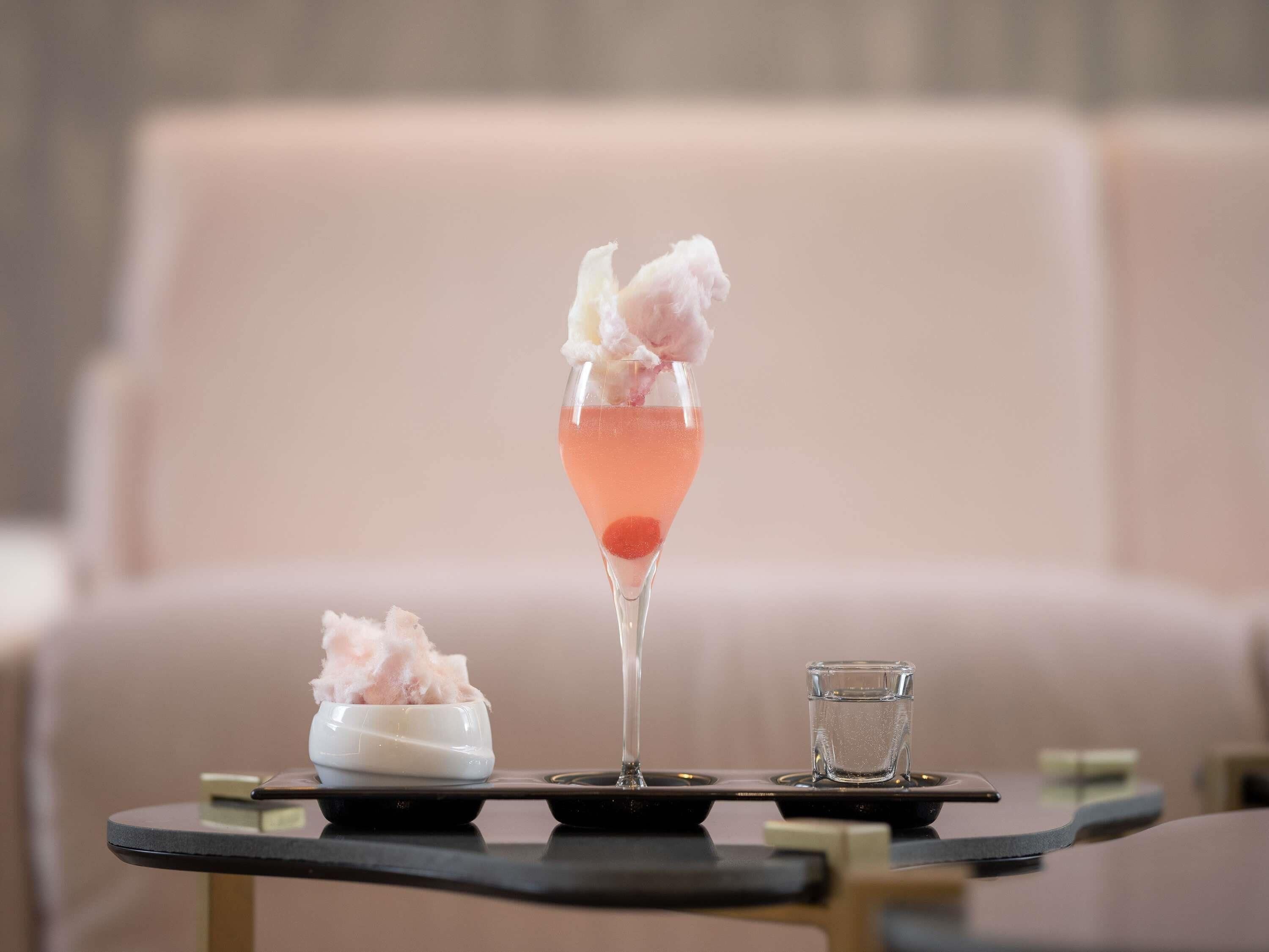 A cocktail glass with a pink drink, a small bowl of ice cream, and a shot glass on a tray.